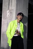 an asian man in a lime colored jacket leaning against a disused building pillar looking very handsome photo