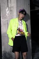an asian man in a lime colored jacket leaning against a disused building pillar looking very handsome photo