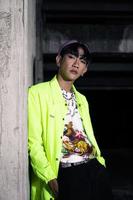 an asian man in a lime colored jacket leaning against a disused building pillar looking very handsome photo