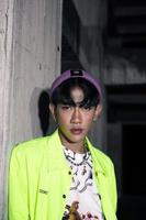 an asian man in a lime colored jacket leaning against a disused building pillar looking very handsome photo