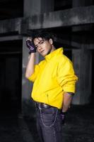 un asiático hombre con pulcro negro pelo vistiendo un amarillo chaqueta y pantalones mientras posando foto