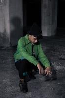 an Asian man squats while wearing a green jacket photo
