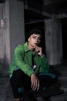 an Asian man squats while wearing a green jacket photo