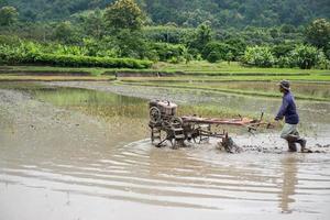 Thai farmers working with a handheld motor plough in a rice field photo