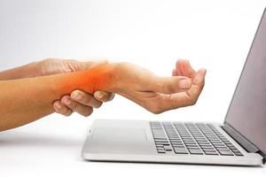 Woman with wrist pain while working on laptop on white background. Healthcare and office syndrome concept. photo