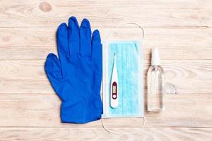 Top view of latex gloves, bottle of alcohol hand sanitizes, medical mask and digital thermometer on wooden background. Antibacterial virus protection concept with copy space photo