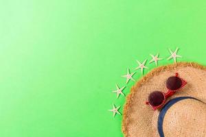 Summer holiday background with straw hat and seashells on green background top view with copy space photo