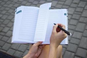 muchachas manos con bolígrafo escritura en cuaderno en parque foto