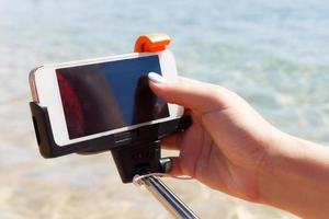 girl adjusts camera on selfie stick in the sea photo