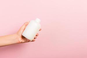 Female hand holding cream bottle of lotion isolated. Girl give tube cosmetic products on pink background photo