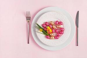 Happy Easter. Table setting for Easter holiday. Easter eggs, duck, flower and cutlery on pink background. Top view, flat lay photo