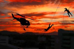 Silhouette Soldiers rappel down to attack from helicopter with sunset and copy space add text photo