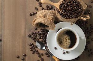 Hot black coffee on cup and roasted coffee beans in wood scoop on old wood background, top view and copy space for text photo