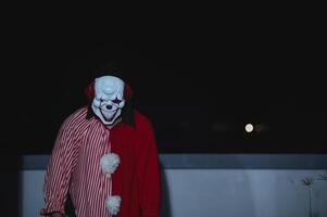 Asian handsome man wear clown mask with weapon at the night scene,Halloween festival concept,Horror scary photo of a killer in orange cloth,Evil clown charactor