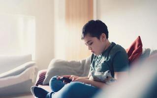 educación concepto,escuela niño utilizando móvil teléfono preparando historia desde internet, chico estudiando en línea aprendizaje a hogar, niño utilizando célula teléfono jugando juego o chateando con amigos, educación en el hogar foto