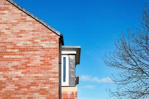 House roof gable end red brick over deep blue sky, Side of House from exterior with branches tree and Spring sky,Mordern English house brick wall texture pattern photo