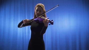 el violinista mujer obras de teatro el violín en etapa y ama su Arte. el joven músico mujer jugando el violín es ejecutando su Arte en el escenario, haciendo el violín hablar. video