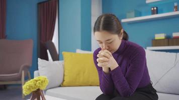 Asian woman is sitting in the living room, anxious and worried. Young Asian woman is sitting at her home worried and thoughtful. video