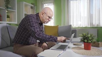 oud Mens gebruik makend van laptop Bij huis nemen notities. oud Mens gebruik makend van laptop Bij huis, aan het doen Onderzoek, boodschappen doen online, berekenen huishouden begroting. video