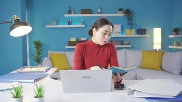 Aziatisch jong vrouw werken van huis bedachtzaam nemen aantekeningen en werken van laptop. video