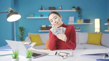 joven asiático mujer es contento mirando a el dinero ella gana a hogar. contento asiático mujer contando dinero ganado a hogar, mirando a monedas