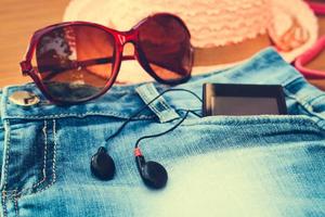 Summer women's accessories red sunglasses, denim shorts, mobile phone, headphones, sun hat. Toned image. photo
