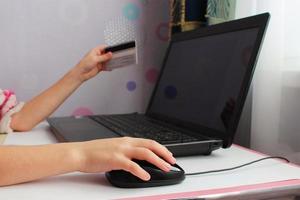 cerca arriba de hembra mano en computadora ratón y participación un crédito tarjeta. el concepto de en línea compras. foto