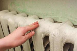 The radiator in the living room. Female hand senses the temperature of the battery. photo