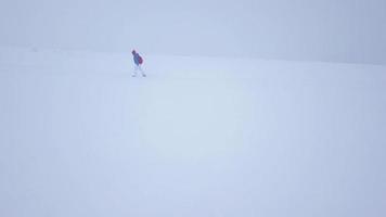 flyg över de ensam turist flicka gående längs de topp av en berg täckt med snö. obekväm ovänlig vinter- väder. video