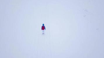 volo al di sopra di il solitario turista ragazza a piedi lungo il superiore di un' montagna coperto con neve. scomodo scortese inverno tempo atmosferico. video