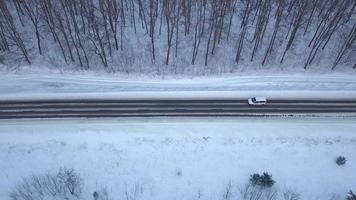 Aerial view on car driving through winter forest road. Scenic winter landscape video