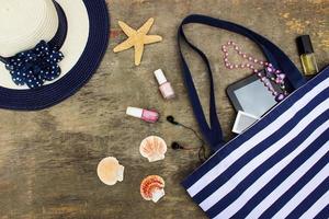 Beach bag, sun hat, cosmetics, mobile phone, tablet, seashells headphones and beads on old wooden background. photo