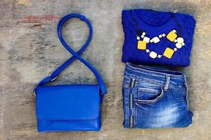 Women's autumn clothing and accessories blue sweater, jeans, handbag, beads on wooden background. Top view. photo