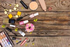 Cosmetics mascara, beads, elastic hair band, false eyelashes, concealer, nail polish, perfume, eyeliner, powder, lip gloss, eye shadow and yellow flowers on wooden background. Top view photo