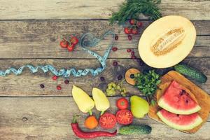 Fruits, vegetables and in measure tape in diet on wooden background. Toned image. photo