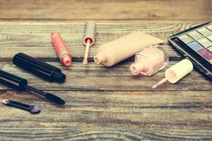 Cosmetics mascara, concealer, nail polish, perfume, lip gloss and eye shadow on wooden background. Toned image. photo