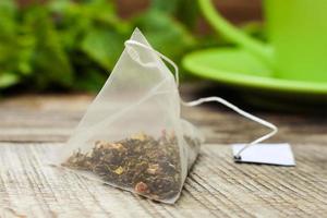 Tea bag on background of mint and and green cup photo
