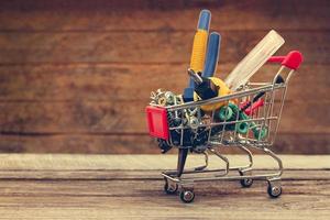 Shopping cart with construction tools on the old wood background. Toned image. photo