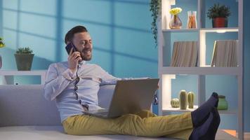 feliz elegante homem de negocios trabalhando remotamente em computador portátil conectados às casa e falando em amigáveis telefone. bonito e carismático homem de negocios olhando às computador portátil e fazer Diversão telefone ligar às lar. video