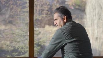 Thoughtful lonely mature man at home looking out the window. Mental health and depression concept. video