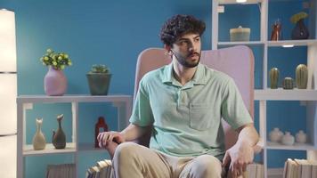 Young man sitting alone at home on sofa and waiting for someone. Thoughtful and unhappy young man in waiting sitting on sofa at home and getting stressed. video