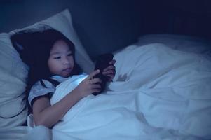 Asian kid playing game on smartphone in the bed at night,The girl Addict social media photo