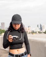 retrato turista joven mujer asiático vistiendo negro sombrero y negro vestir con retro película cámara a tomar fotos. salvar recuerdos de tu viajes foto