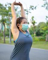 retrato hermosa asiático mujer en ropa de deporte, en pie con su atrás, extensión antes de hacer ejercicio al aire libre en parque Mañana a lograr sano estilo de vida. sano calentamiento arriba foto