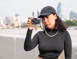 retrato turista joven mujer asiático vistiendo negro sombrero y negro vestir con retro película cámara a tomar fotos. salvar recuerdos de tu viajes foto