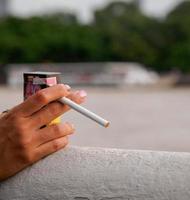 Primer plano mano mujer joven adolescente asia una persona que lleva una camisa negra mantenga fumar cigarrillo color blanco de pie al aire libre junto a la pared foto