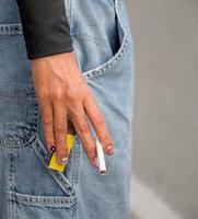 Primer plano mano mujer joven adolescente asia una persona que lleva una camisa negra mantenga fumar cigarrillo color blanco de pie al aire libre junto a la pared foto