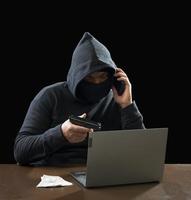 Hacker spy man one person in black hoodie sitting on a table looking computer laptop used login password attack security to circulate data digital in internet network system, night dark background. photo