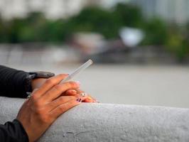 Closeup hand woman teen young asia one person wearing a black shirt hold smoking cigarette white color standing outdoor by the wall photo