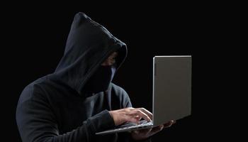 Hacker spy man one person in black hoodie sitting on a table looking computer laptop used login password attack security to circulate data digital in internet network system, night dark background. photo